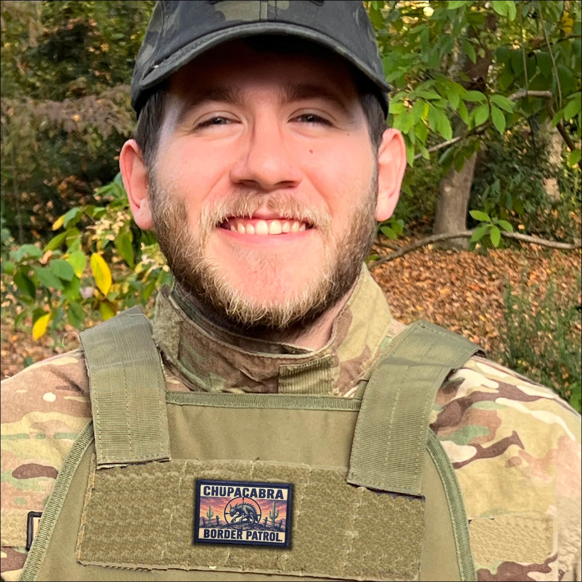 Person wearing a camouflage uniform with a Chupacabra Border Patrol morale patch in an outdoor setting.