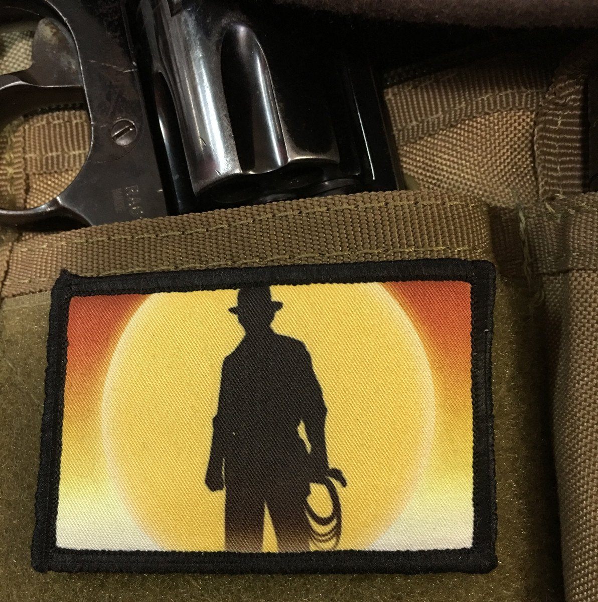 Patch featuring silhouette of iconic Indiana Jones with the sunset in the background. The patch in on a bag holding a revolver.